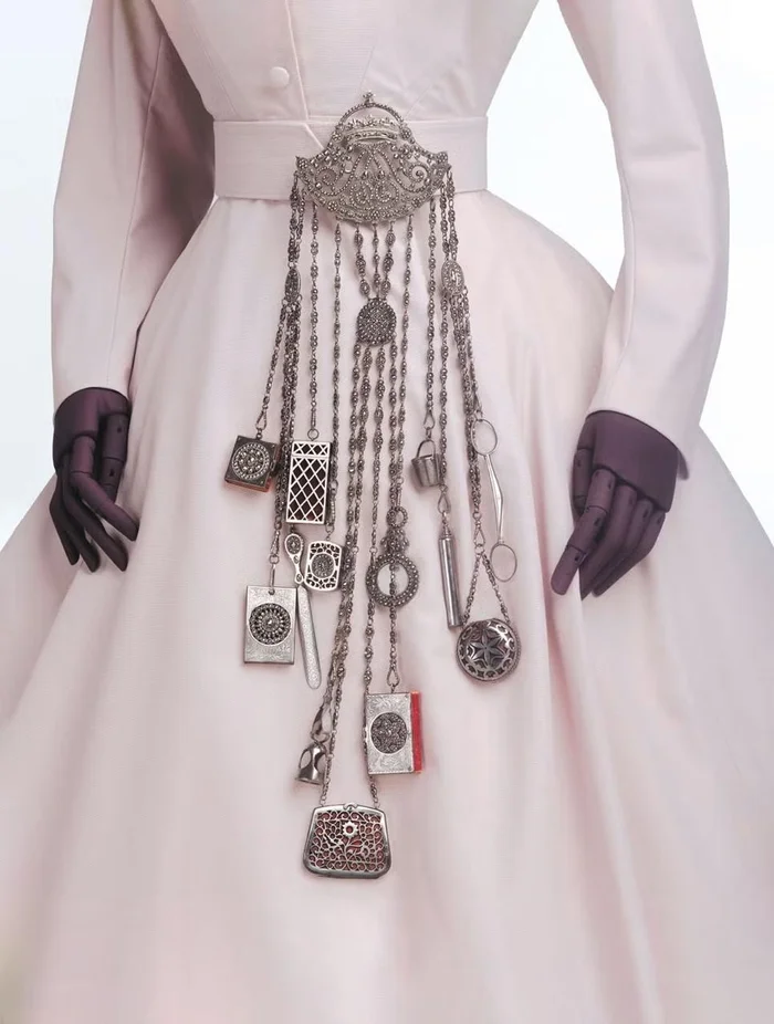 A silver chatelaine worn on a pink dress, with hanging tools and cases