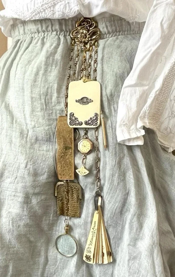 A gold chatelaine with notebook, pencil, magnifying glass, and fan