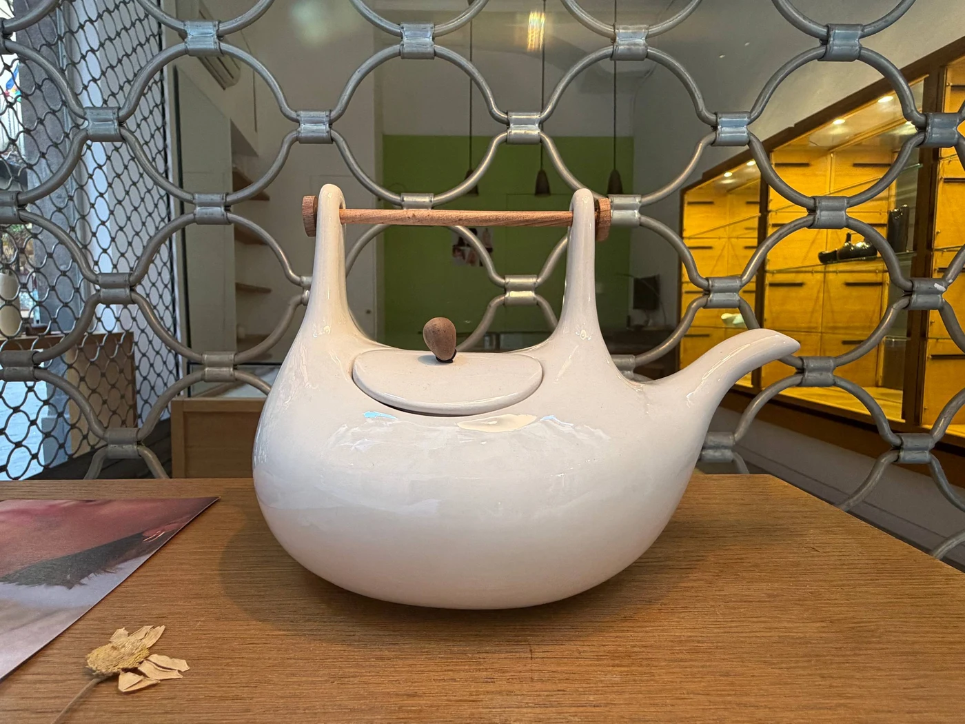 A white ceramic teapot with a wooden handle bar, photographed in the store
